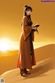 A woman in a brown dress holding a book in the desert.