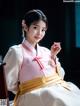 A woman in a pink and white hanbok sitting on a chair.