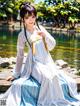 A woman in a blue and white dress sitting by a pond.